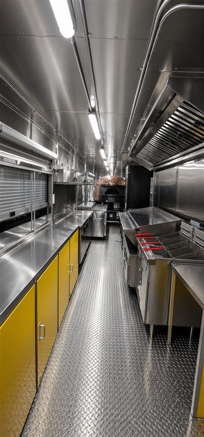 Food truck interior with yellow cabinetry, wood-fired pizza oven and stainless prep line