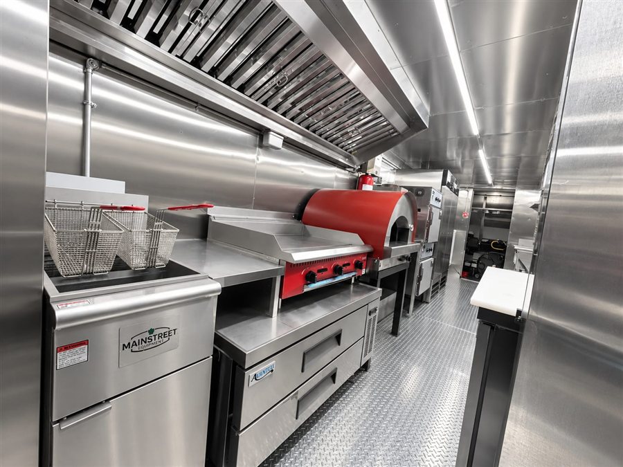 Stainless steel food truck kitchen interior with built-in wood-fired pizza oven and commercial fryer