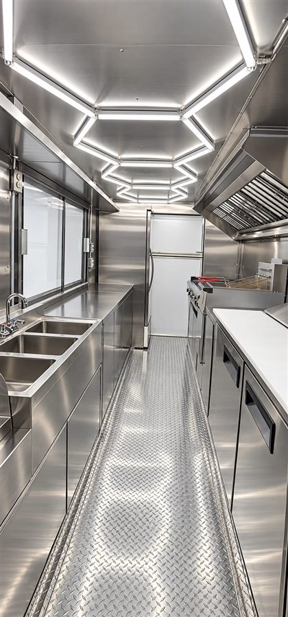 Empty stainless steel food truck kitchen with hexagon LED ceiling lighting and reach-in fridge